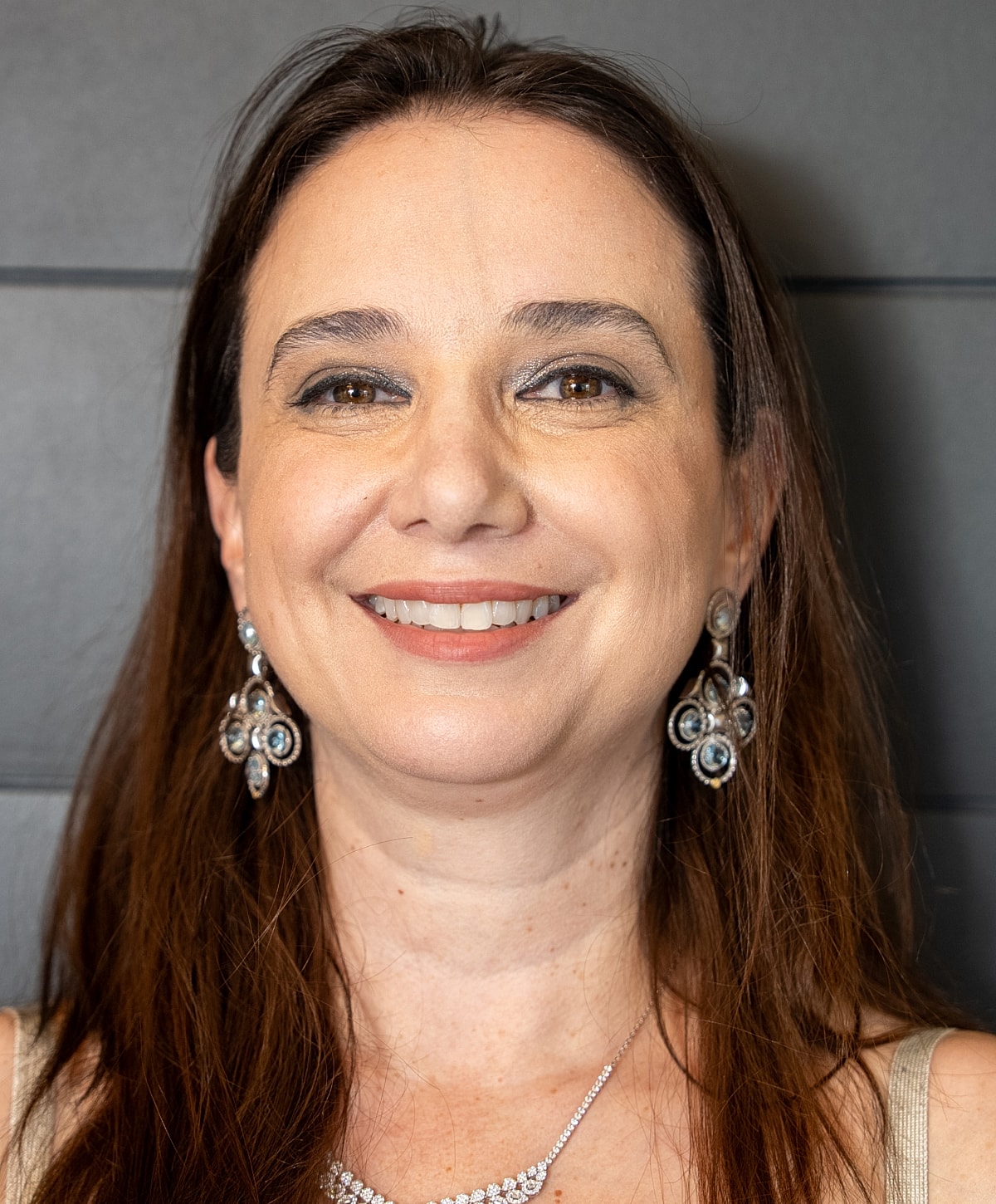 Smiling woman with long hair and elegant jewelry.